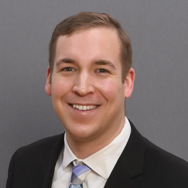 Headshot of Brady Kuennen in black suit, white shirt, and tie
